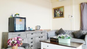Un salón con un sofá gris, una mesa de centro, un televisor sobre un mueble, un cuadro en la pared y un aire acondicionado.