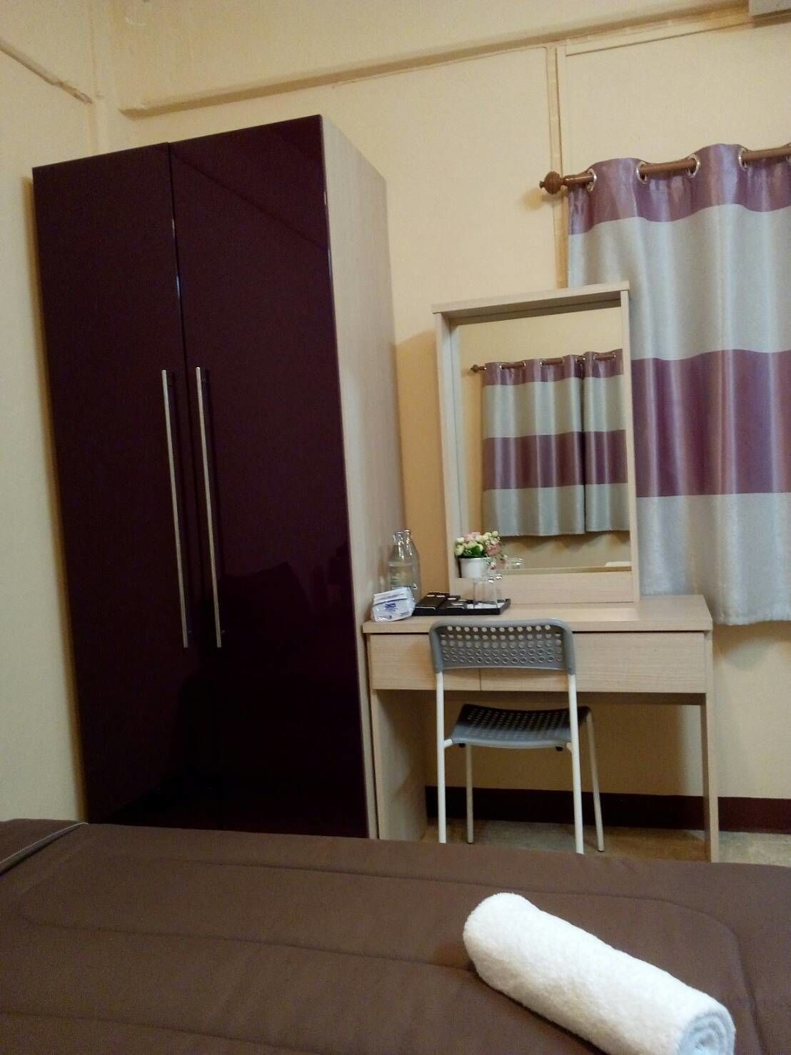A hotel room with a bed, a desk, a chair, a wardrobe, and a bathroom with a striped curtain.
