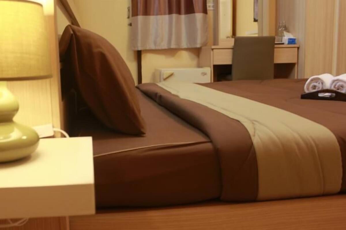A hotel room with a bed, a bedside lamp, a chair, a desk, and a window with curtains.
