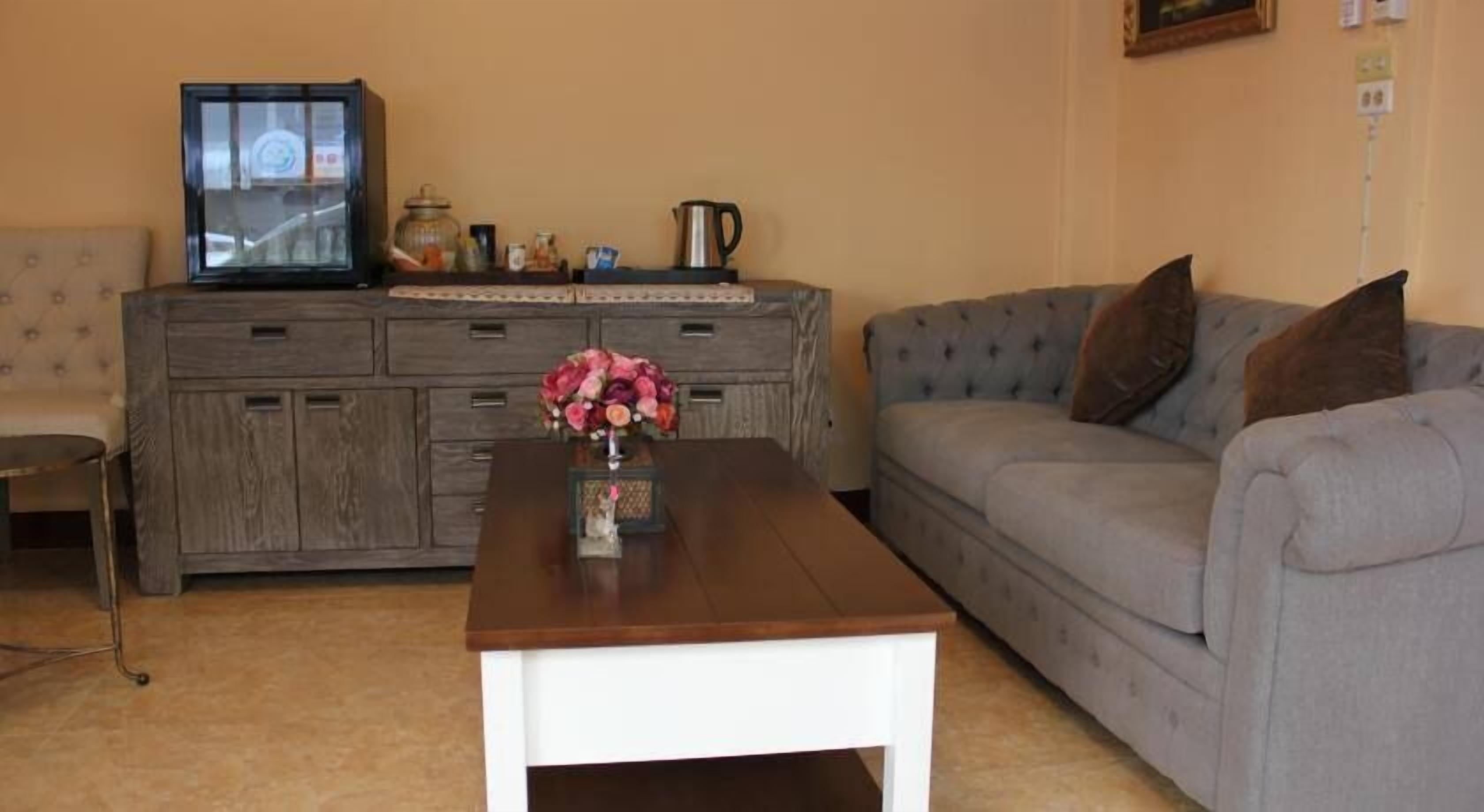 A living room with a wooden coffee table, a grey sofa, a cabinet with kitchen items, and a television on top.