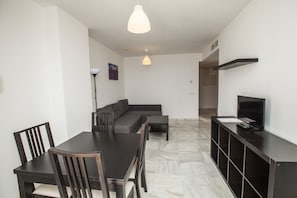 A modern living room with a dark wooden dining table, chairs, a sofa, and a TV on a black stand.