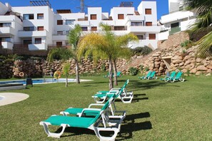 A poolside area with green lounge chairs, a small palm tree, and a rocky hillside. - Resort de Nerja (Nerja)