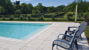 Une piscine dotée d’une terrasse carrelée, entourée d’une clôture verte et d’arbres.