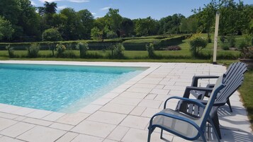 Uma piscina com deck revestido, cercada por uma cerca verde e árvores.