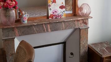 A room with a large mirror, a book titled 'Paradise', a vase with flowers, and a small table with a pink vase.