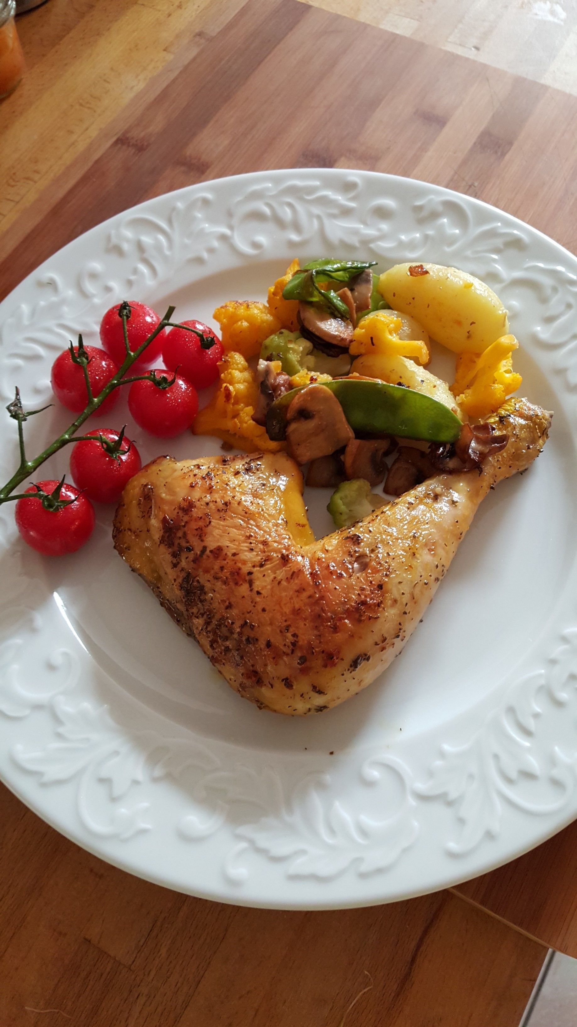Une assiette blanche contenant du poulet rôti, des tomates cerises et un mélange de légumes.