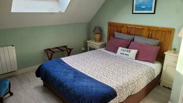 A bedroom with a sloped ceiling, a skylight, a bed with a blue quilt, a nightstand with a lamp, and a poster on the wall.