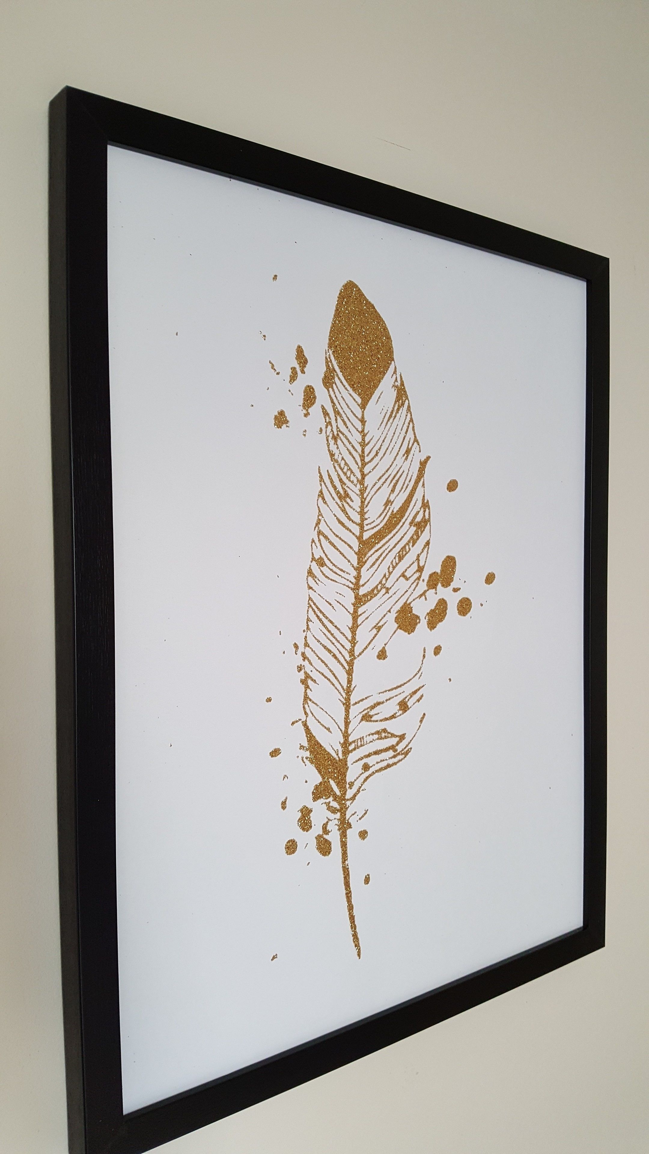 A framed artwork of a feather with gold accents.
