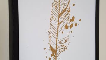 A framed artwork of a feather with gold accents.