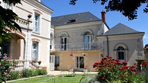 Un bâtiment à deux étages doté d’un balcon, d’un jardin fleuri et d’une table entourée de chaises.