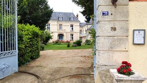 Une entrée fermée par un portail mène à un immeuble. On y voit une plaque portant le numéro « 78 » et une autre plaque ornée d’une croix et d’une inscription.