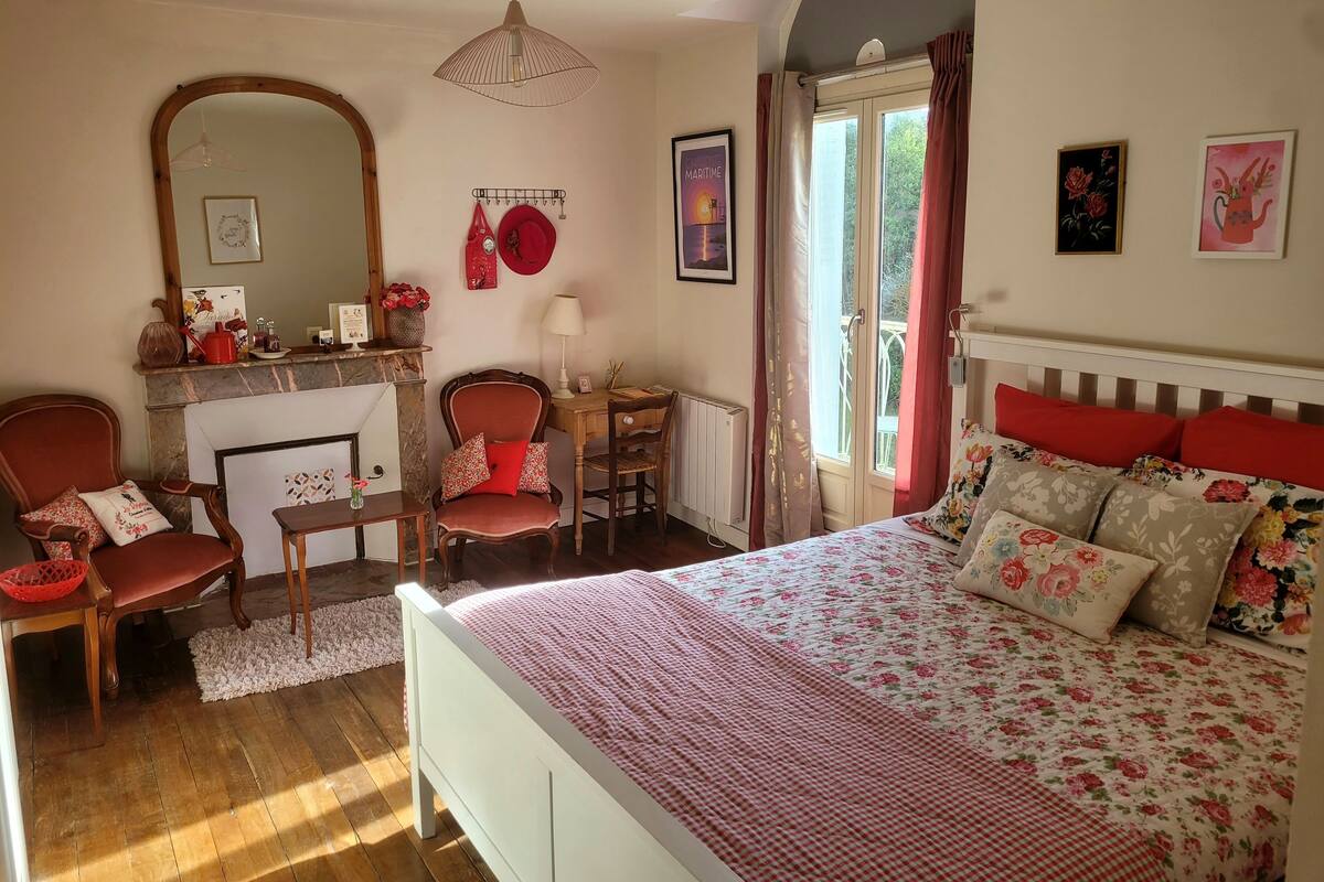 Een slaapkamer met een bed, een stoel, een bureau, een spiegel en een raam met gordijnen.