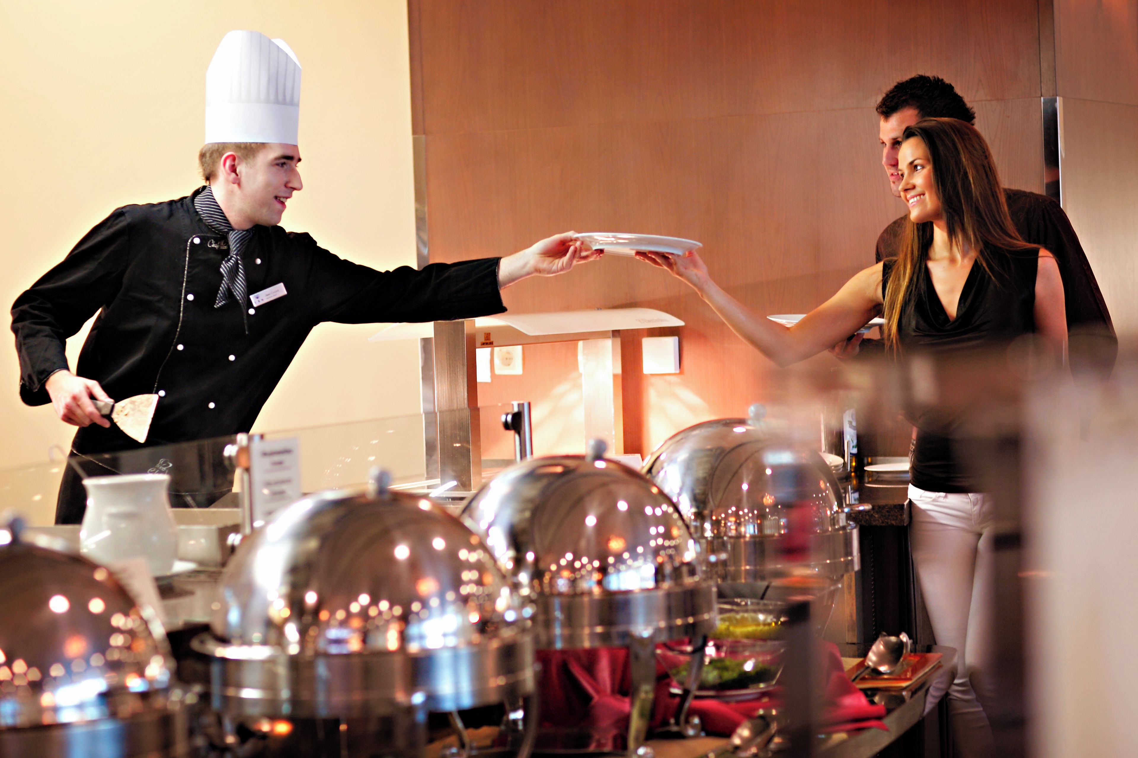 A buffet setup with multiple food stations and a waiter serving a guest.