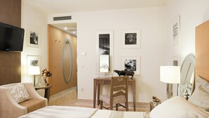 Quarto de hotel com uma cama, uma escrivaninha com cadeira, uma televisão na parede e quadros decorativos.