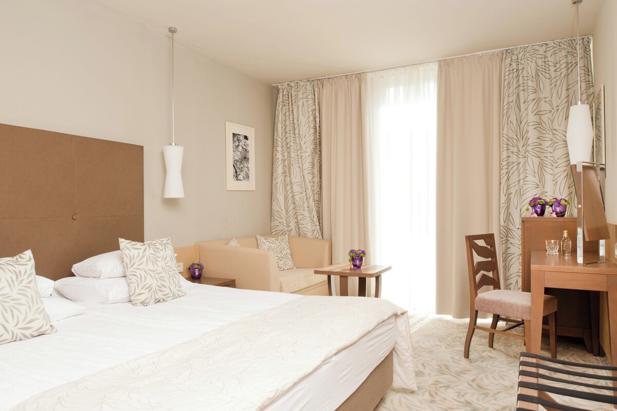 Habitación de hotel con una cama grande, un escritorio, una silla, un televisor y una ventana con cortinas.