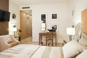 Habitación de hotel con cama, escritorio con silla, televisor montado en la pared y cuadros enmarcados.