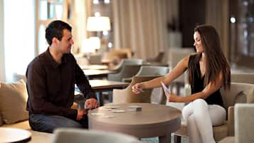 Un hombre y una mujer sentados en una mesa redonda en el vestíbulo de un hotel, con un sofá y sillas alrededor.