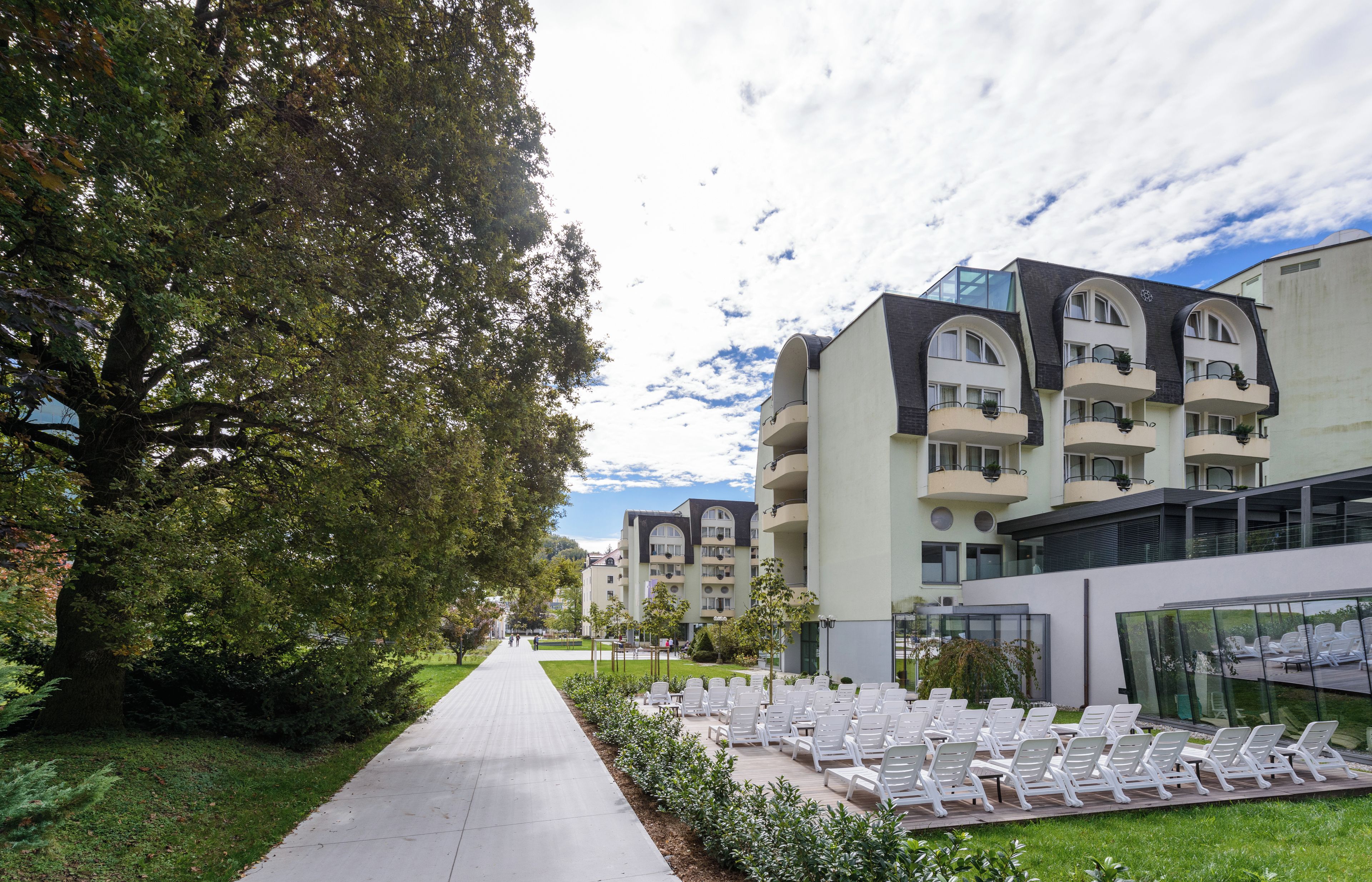 A pathway leading to a building with multiple balconies and a garden area with sun loungers.