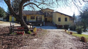 A yellow building with a tiled roof, a large tree in front, and a gravel driveway. - B&B La Grotta (Castel Giorgio)