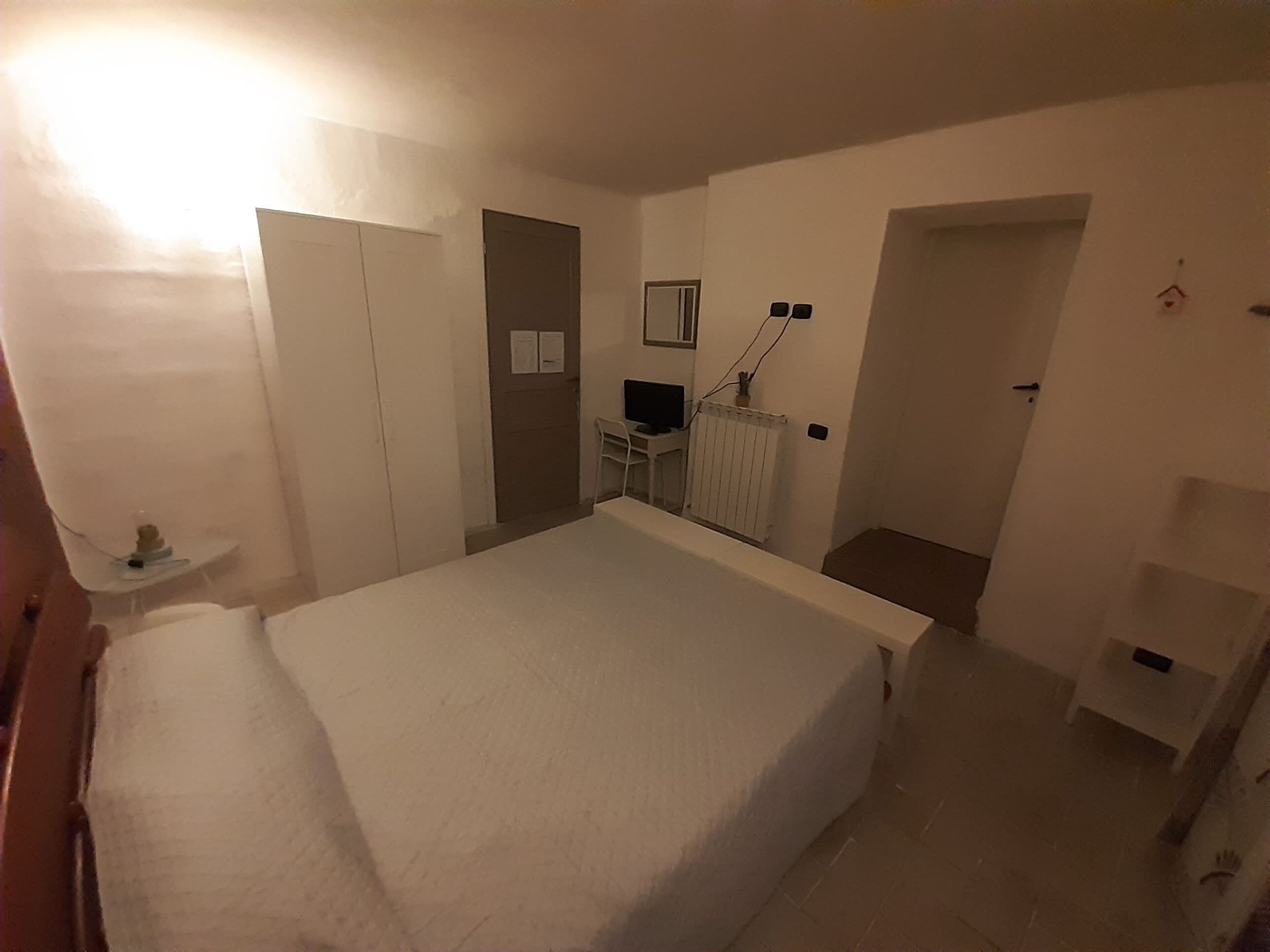 A bedroom with a bed, a desk, a chair, a radiator, and a door.