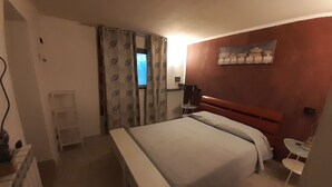 A hotel room with a bed, a small bedside table, a chair, a window with curtains, and a wall-mounted artwork. - B&B La Grotta (Castel Giorgio)