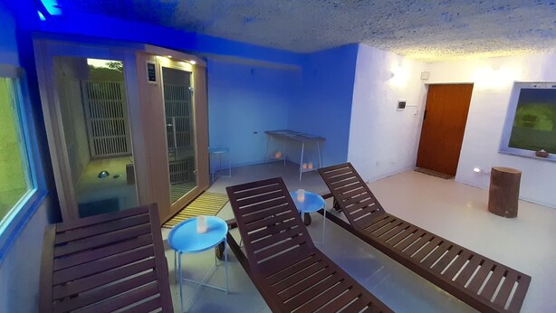 A room with two wooden loungers, a small table, and a chair. There is a glass door leading to a balcony with a view of trees. - B&B La Grotta (Castel Giorgio)