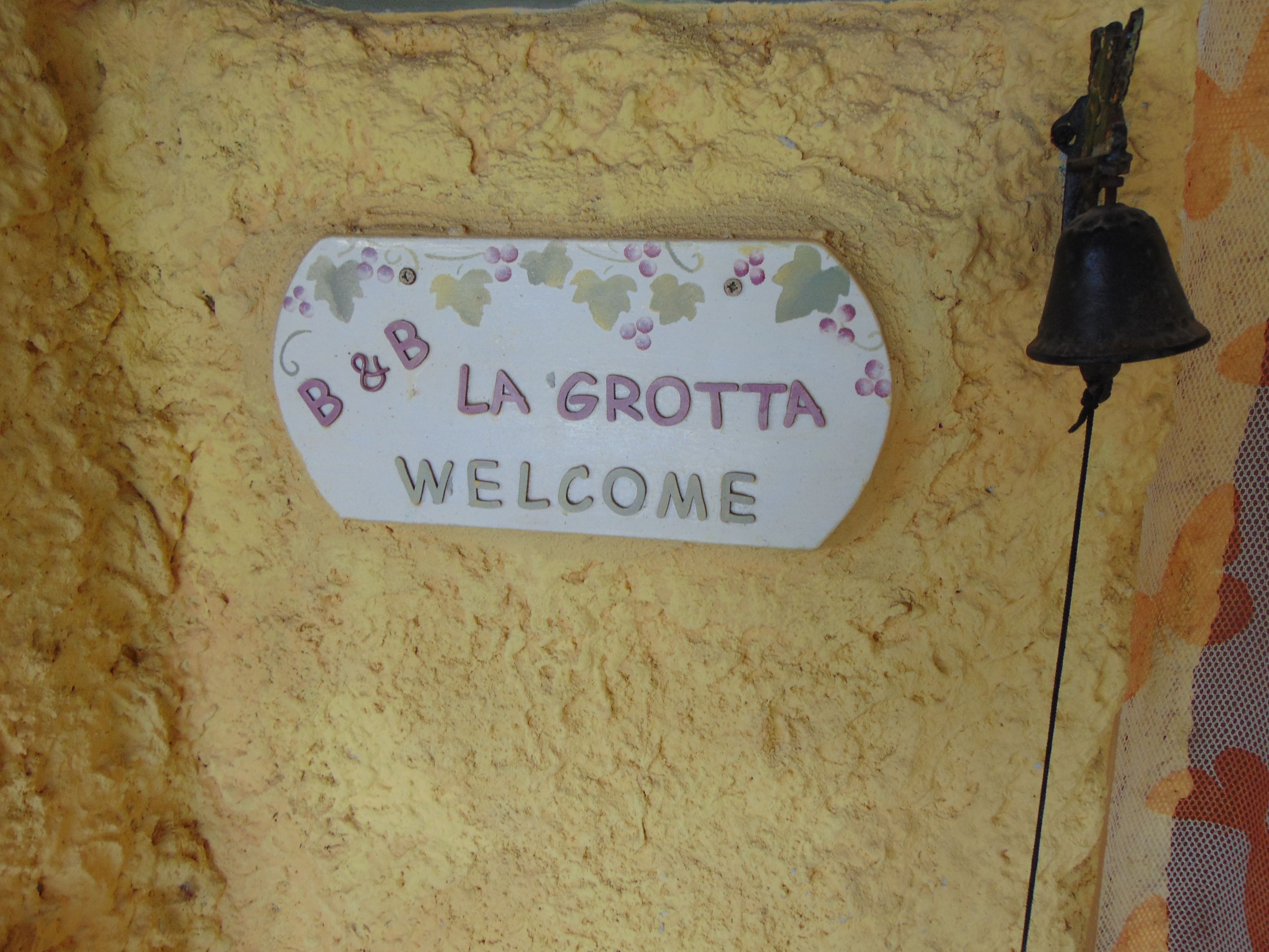 En välkomstskylt med texten ”B&B LA GROTTA” och en klocka på en vägg med en intressant yta.