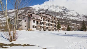 A multi-story hotel with balconies, set against a snowy mountain backdrop. - Hotel Du Park (Opi)