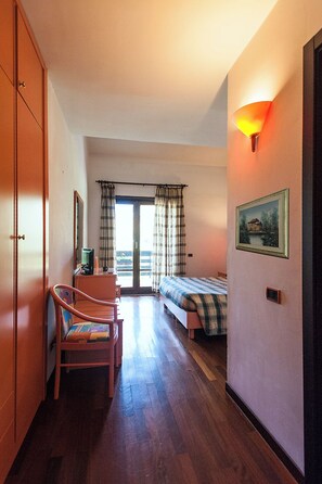 Habitación de hotel con cama, escritorio, silla, ventana con cortinas y lámpara de pared.