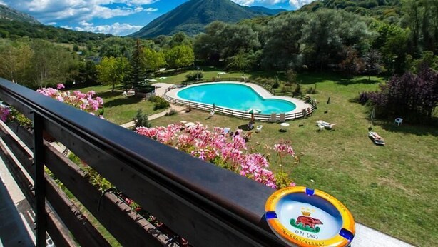 A pool surrounded by a fence, with a mountainous backdrop and a balcony railing in the foreground. - Hotel Du Park (Opi)