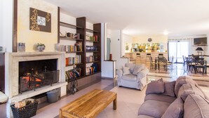 A living room with a fireplace, bookshelves, a sofa, and a dining area. - Hotel Du Park (Opi)