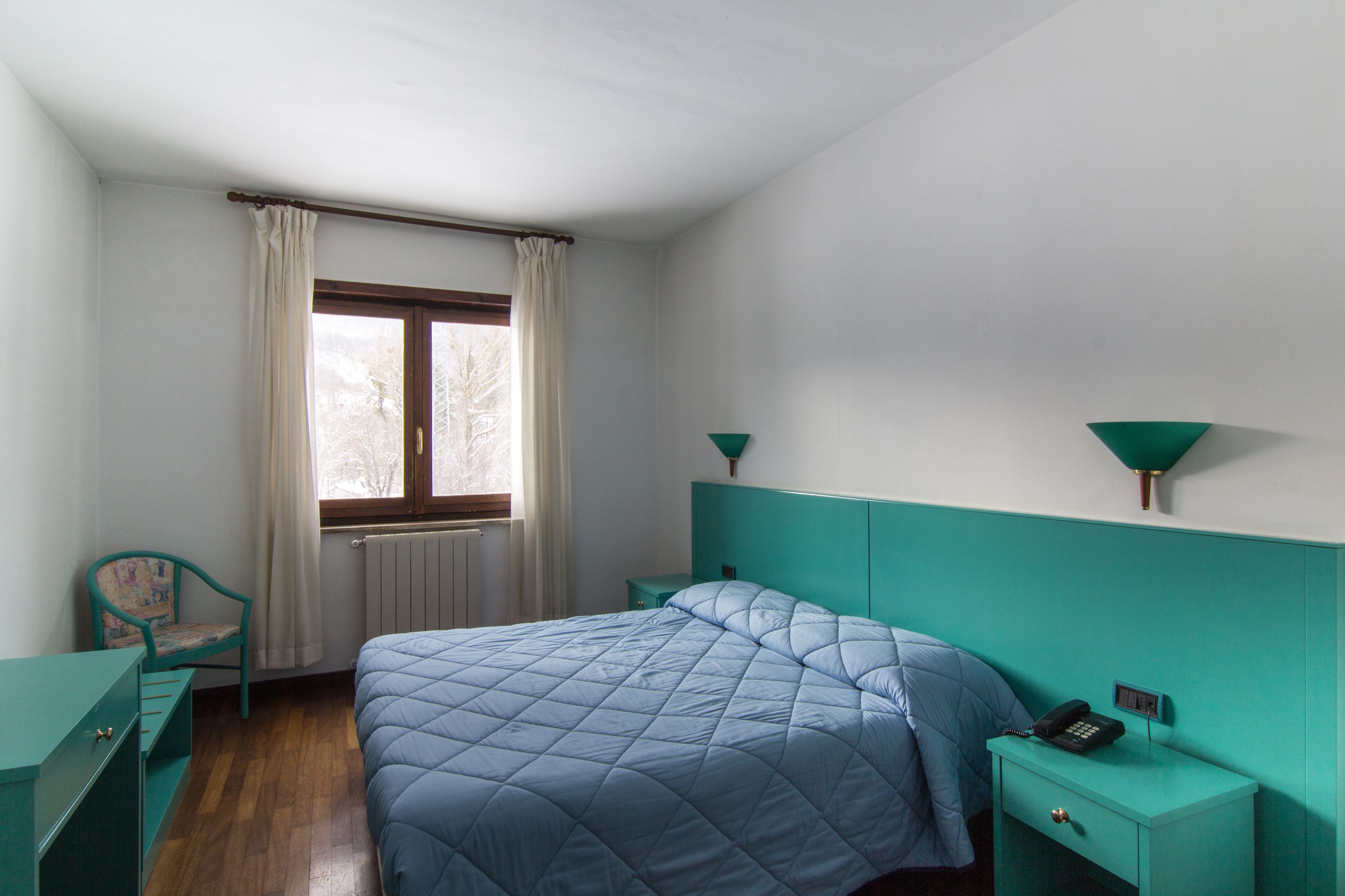 Una camera da letto con un letto, una sedia, un comodino e una finestra con tende.