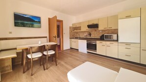 A compact kitchen with a dining area, wooden cabinets, and a white refrigerator. - Aparthotel Buchauer Tirol (Thiersee)