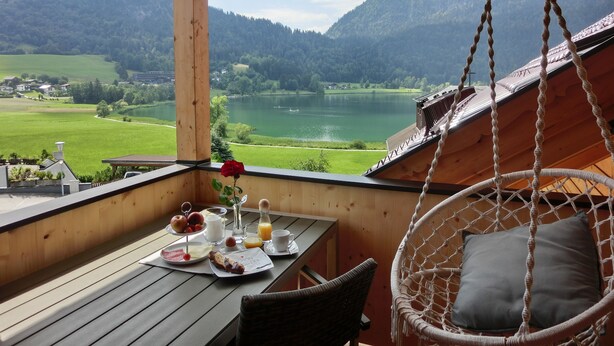 A wooden deck with a table set for breakfast, overlooking a lake and mountains. - Aparthotel Buchauer Tirol (Thiersee)