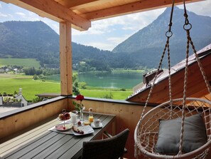 Una terraza de madera con una mesa dispuesta para el desayuno, con vista a un lago y montañas.