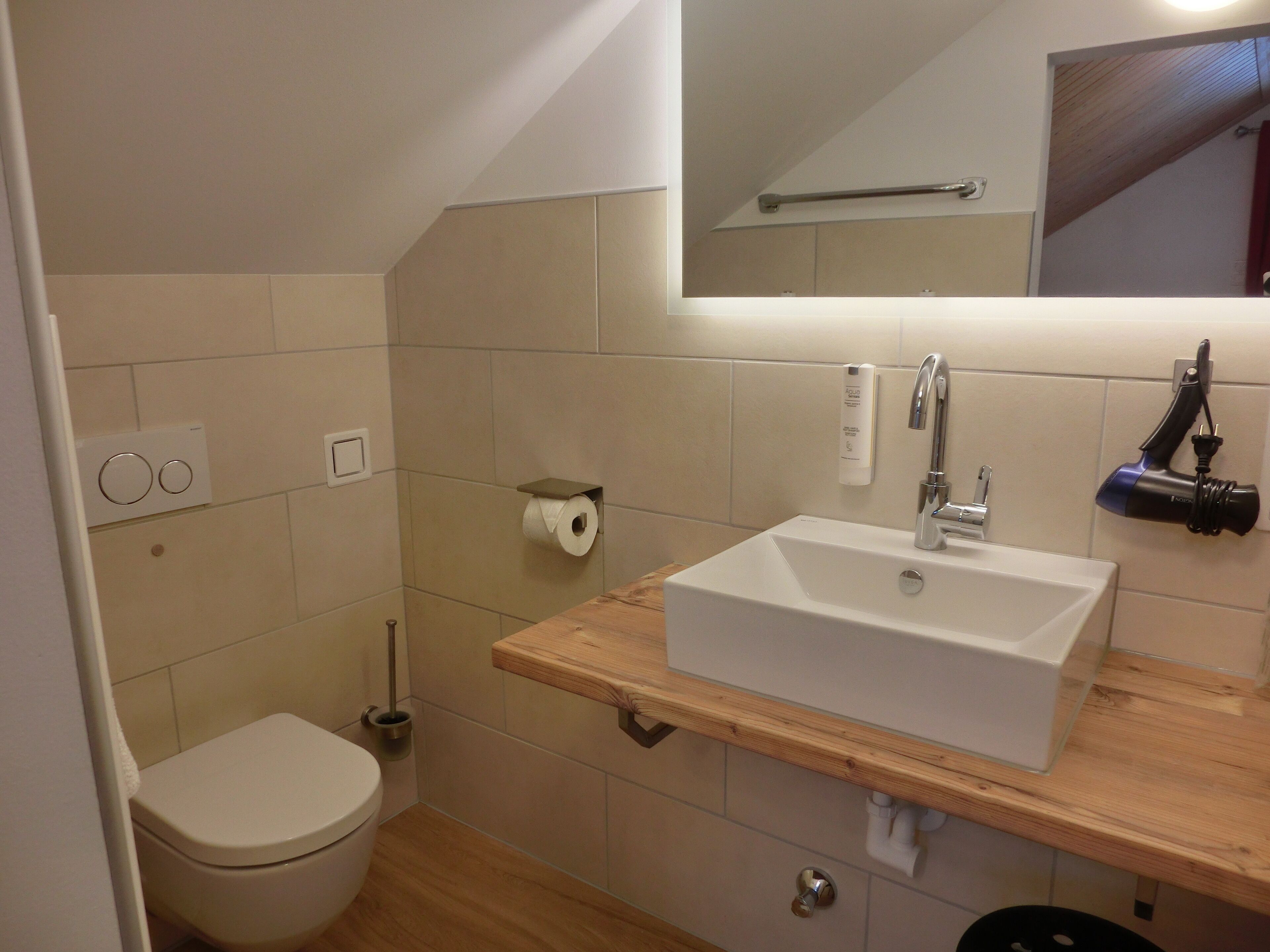 A modern bathroom with a white sink, wooden countertop, and a mirror above the sink.