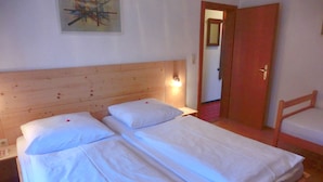 A room with two single beds, a wooden headboard, a nightstand with a lamp, and a door leading to another room. - Buchauer-Tirol Landhaus Buchauer (Thiersee)