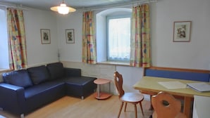 A cozy living room with a dark blue sofa, a wooden dining table, and a small round table. - Buchauer-Tirol Landhaus Buchauer (Thiersee)
