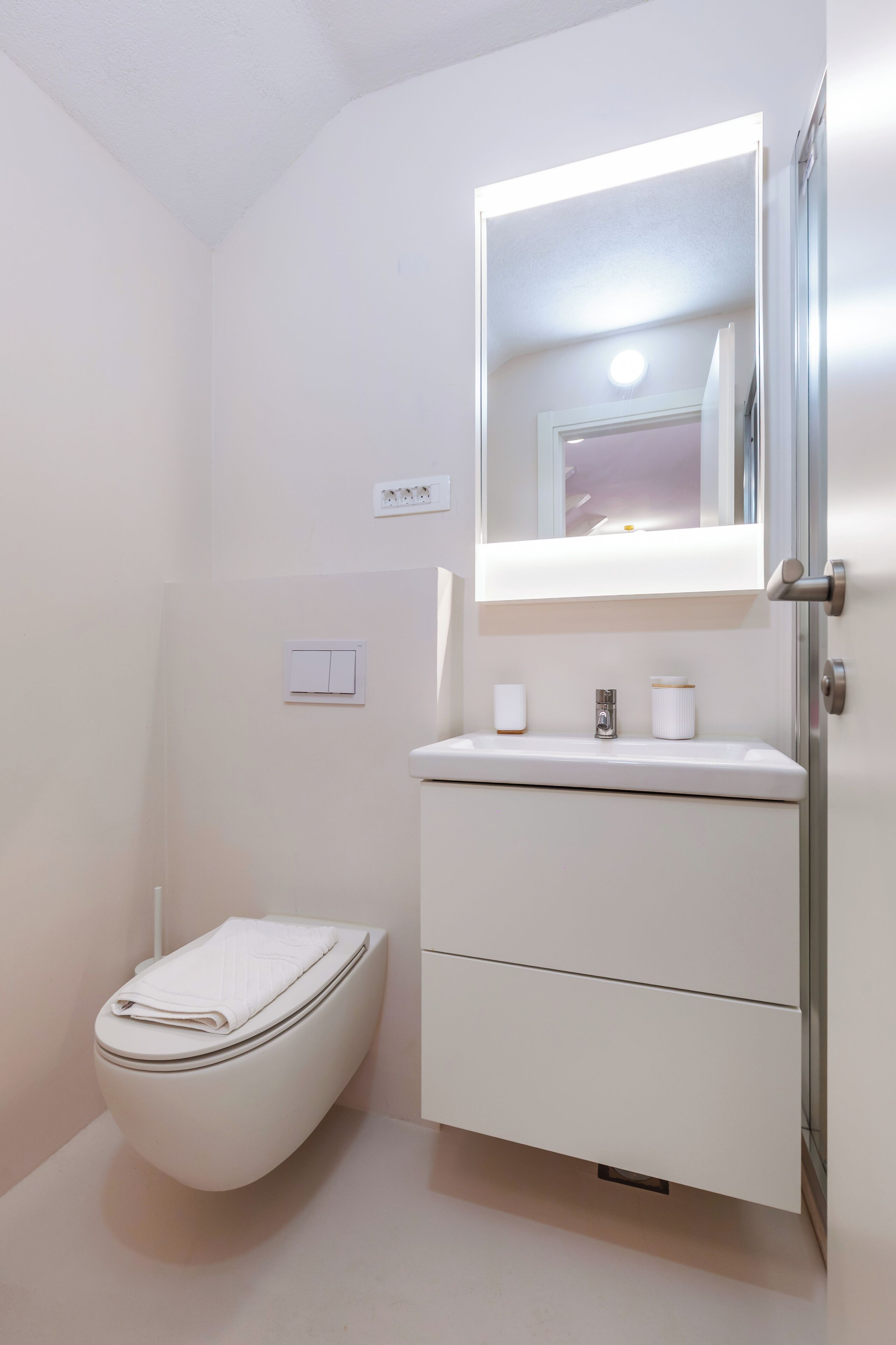 Een badkamer met toilet, wastafel, spiegel en lichtschakelaar.