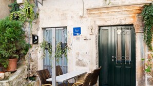 Un edificio in pietra con una porta verde scuro, un tavolo con sedie in vimini e piante in vaso.