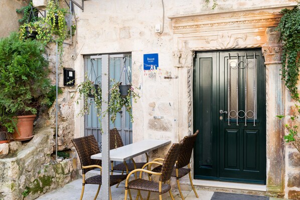 A stone building with a dark green door, a table with wicker chairs, and potted plants. - Booba Rooms (Dubrovnik)