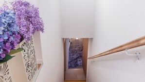 Una escalera estrecha con bordes amarillos, paredes blancas y un espejo decorativo a la izquierda.