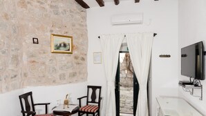 Una stanza con pareti in pietra, soffitto in legno, televisione, tavolo con sedie e finestra con tende.
