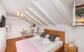 A bedroom with a bed, bedside table, lamp, and a view of a village through a window.