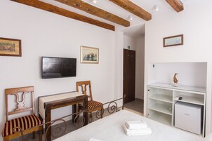 Quarto de hotel com cama, escrivaninha, cadeira, televisão e um pequeno frigorífico.