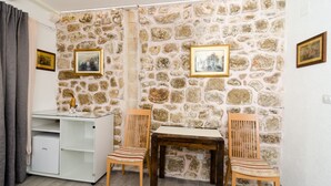 Una stanza con una parete in pietra, due sedie di legno, un tavolino e un armadietto bianco.
