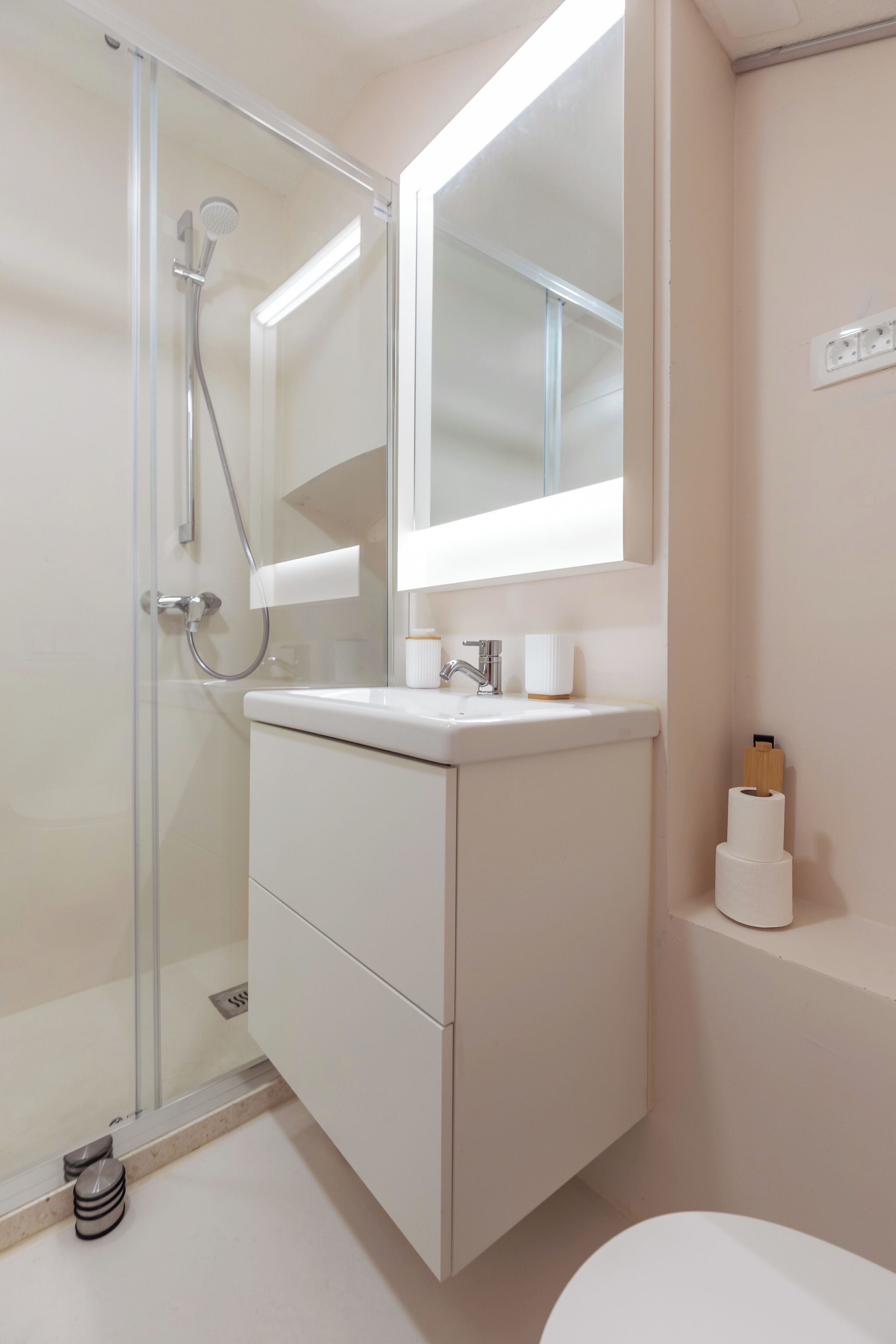 Un baño con cabina de ducha de vidrio, un lavabo blanco, un espejo sobre el lavabo y un inodoro.