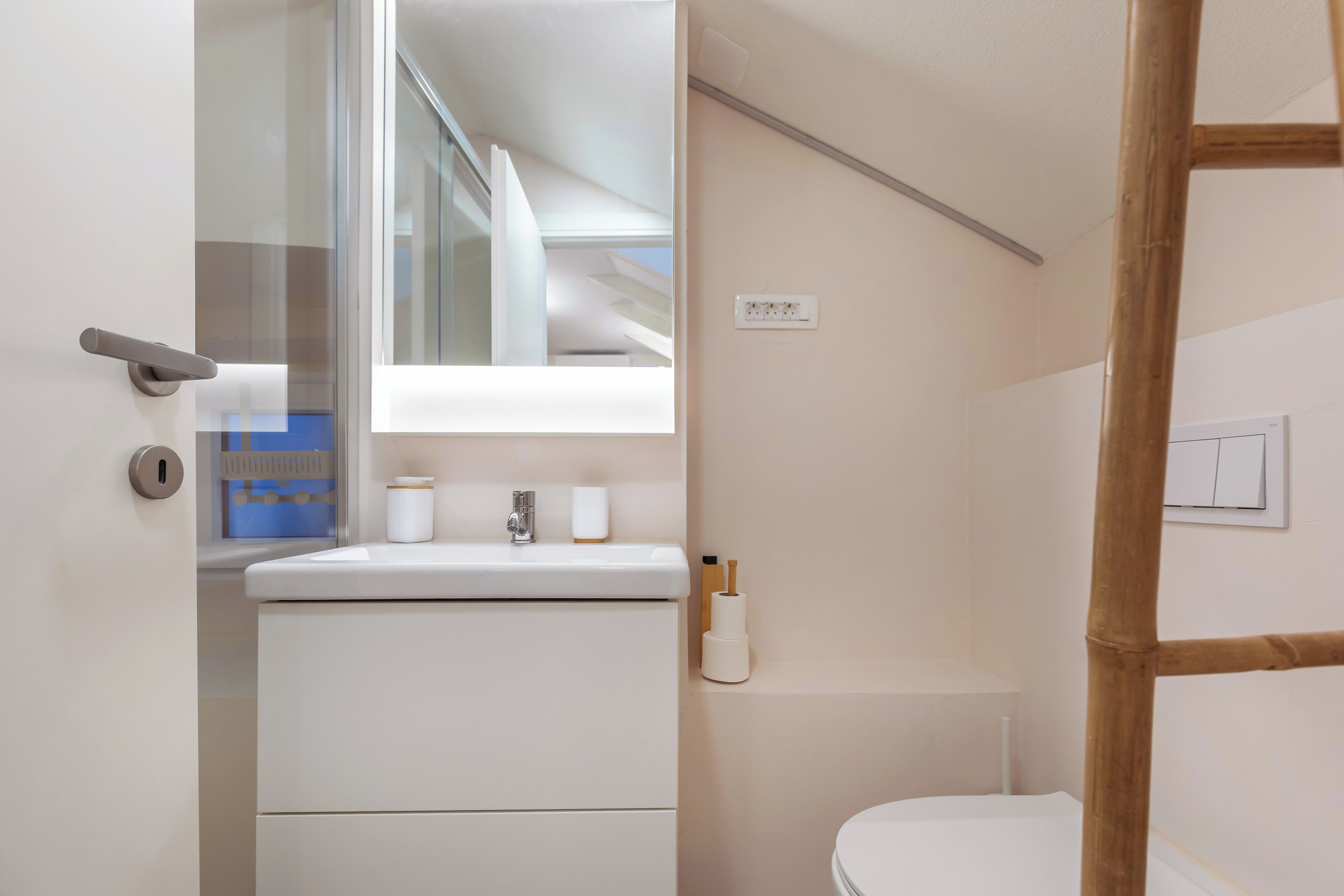 Une salle de bain avec un lavabo blanc, des toilettes et une fenêtre située au-dessus du lavabo.