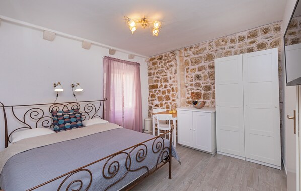 A bedroom with a bed, a desk, a chair, a wardrobe, and a stone wall. - Booba Rooms (Dubrovnik)