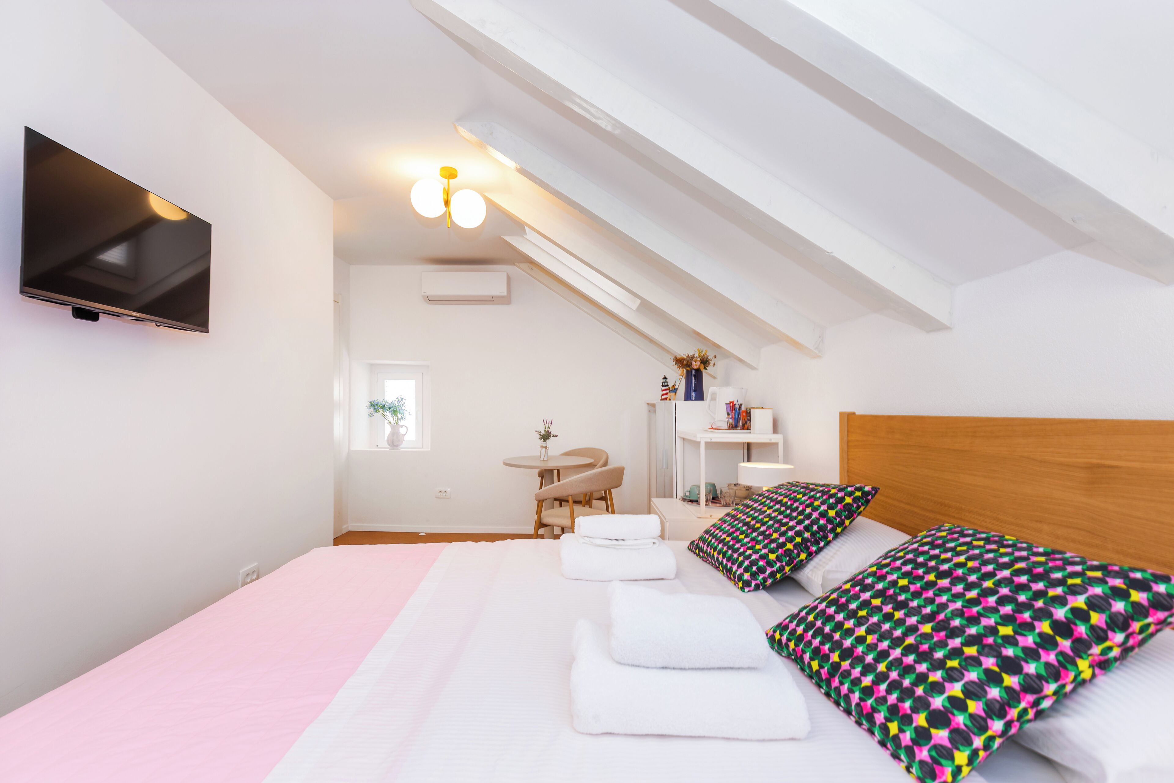A bedroom with a bed, pillows, a TV, a desk, and a chair.